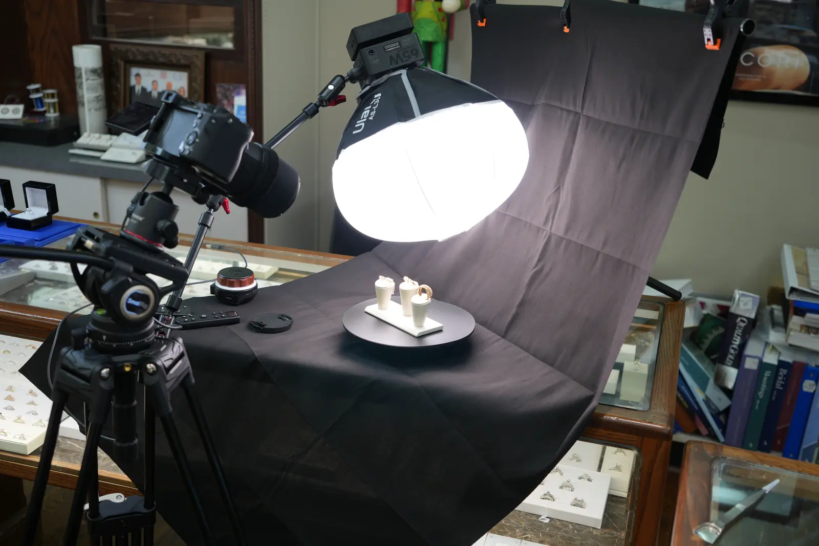 Shoot-day setup at O'Neal's Jewelers: a camera on a tripod aimed at ring stands on a turntable, lit by a round softbox
