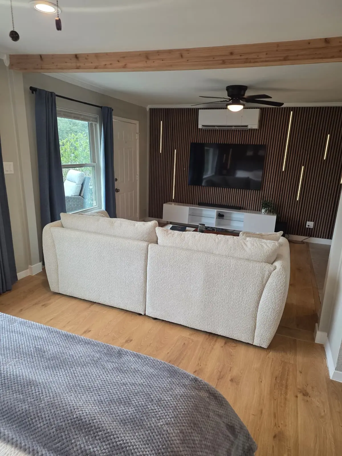 Living room at The McCosh Apartment with a cream sofa, a TV wall with wood slats and light wood floors